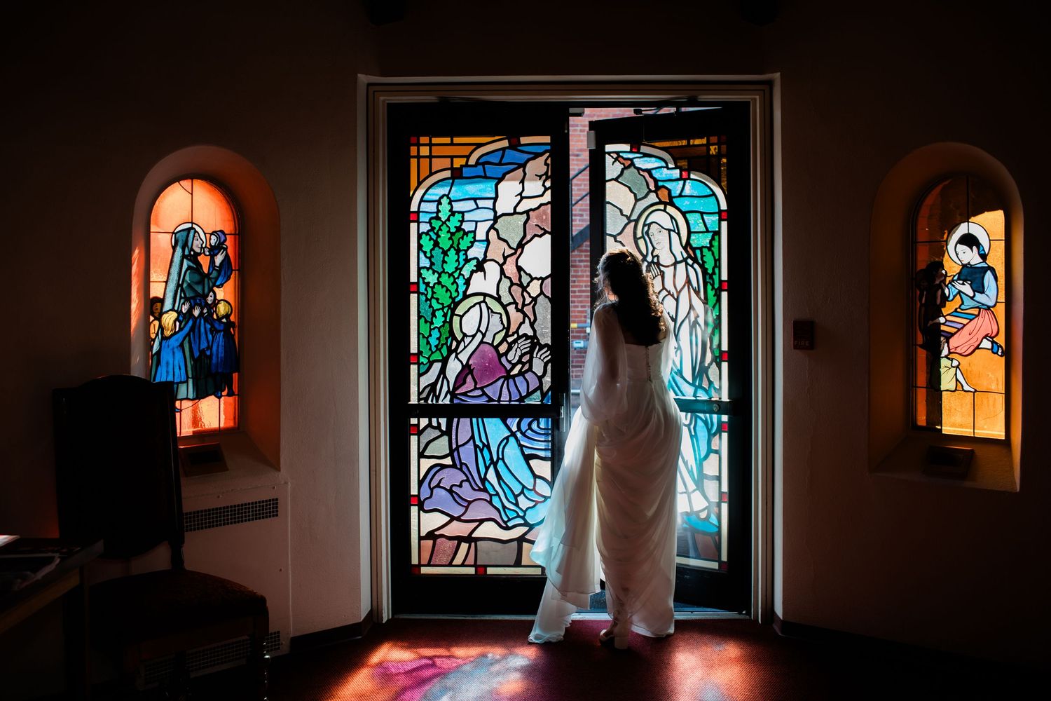 Mystical stained glass windows illuminate a dark church hallway with dramatic lighting.
