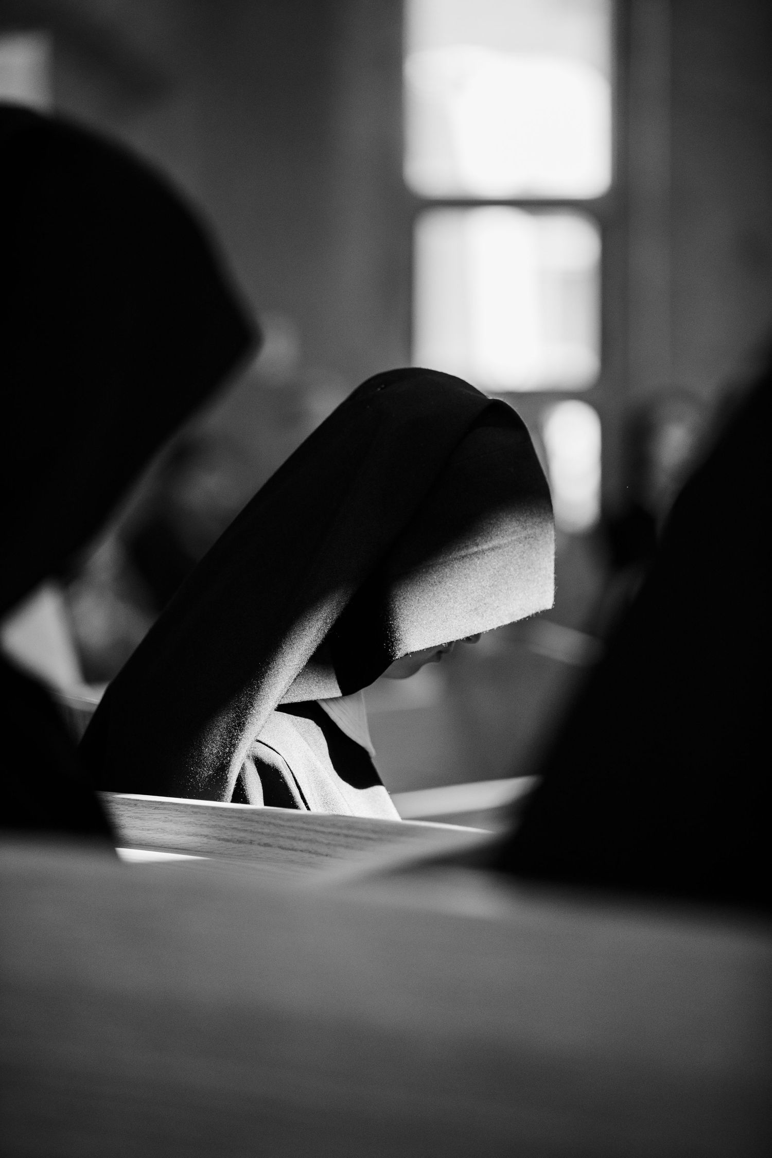 Black and white photo of a nun in habit reading a book, with soft light from a window in the background.
