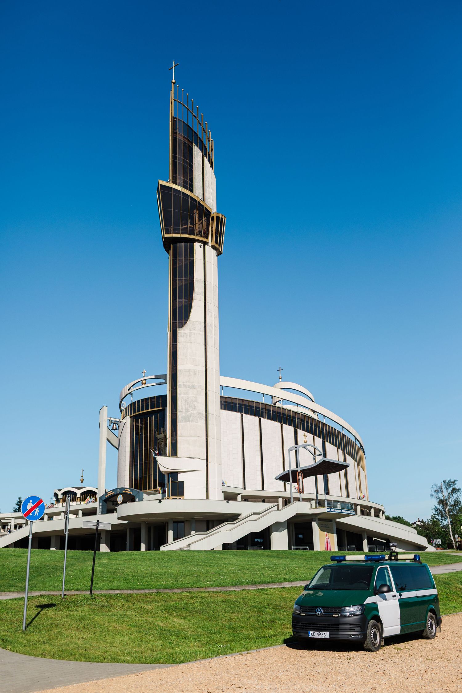 Modern circular Catholic church with tall tower and green van in Krakow, Poland.