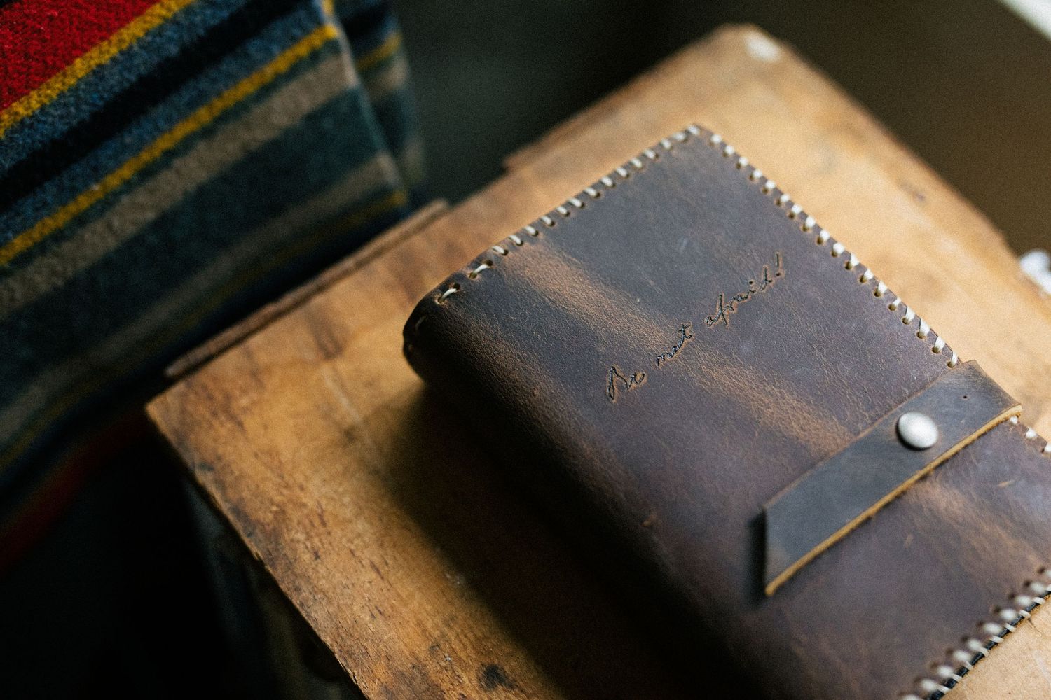 A handcrafted dark brown leather wallet with stitched edges rests on a wooden surface.