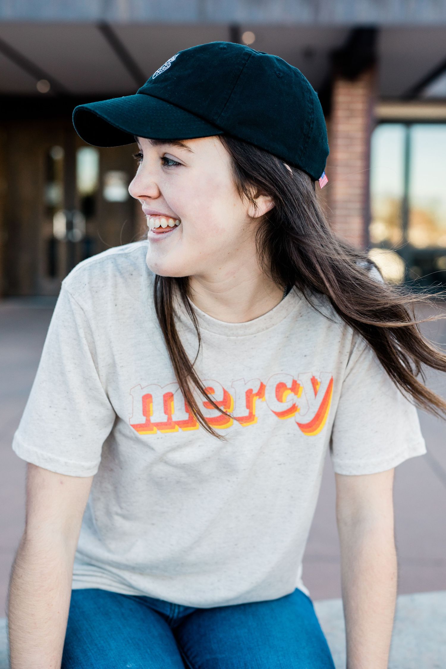 Woman wearing white t-shirt and baseball cap smiles while looking down in casual portrait series.