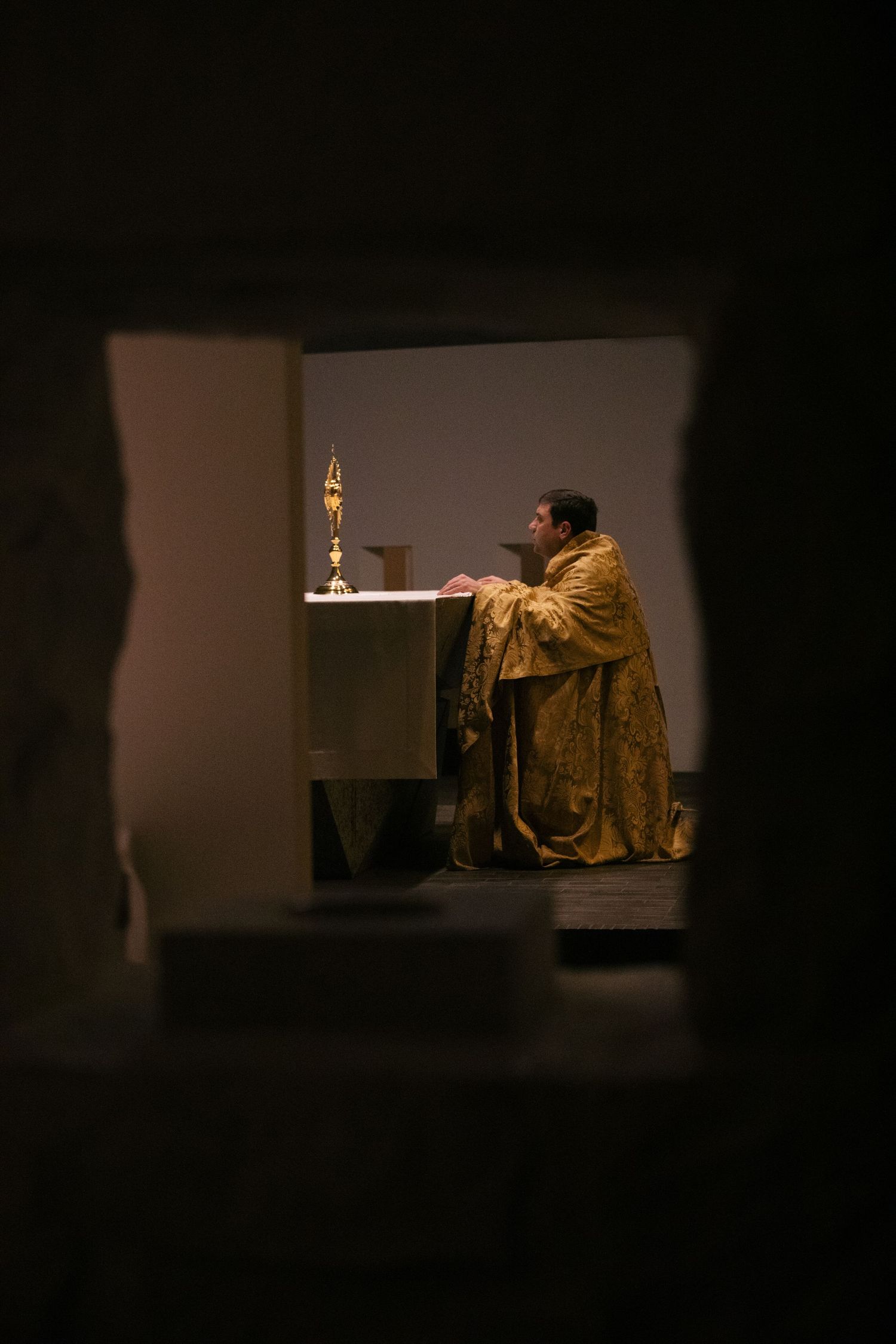 Dramatic lighting illuminates a solitary figure in a dark room sitting at a dimly lit table.