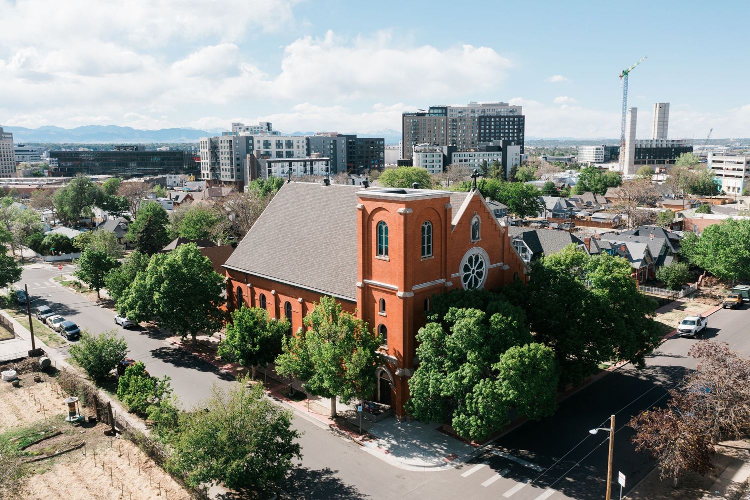 Aerial view of a historic red brick church surrounded by trees in a modern urban cityscape.