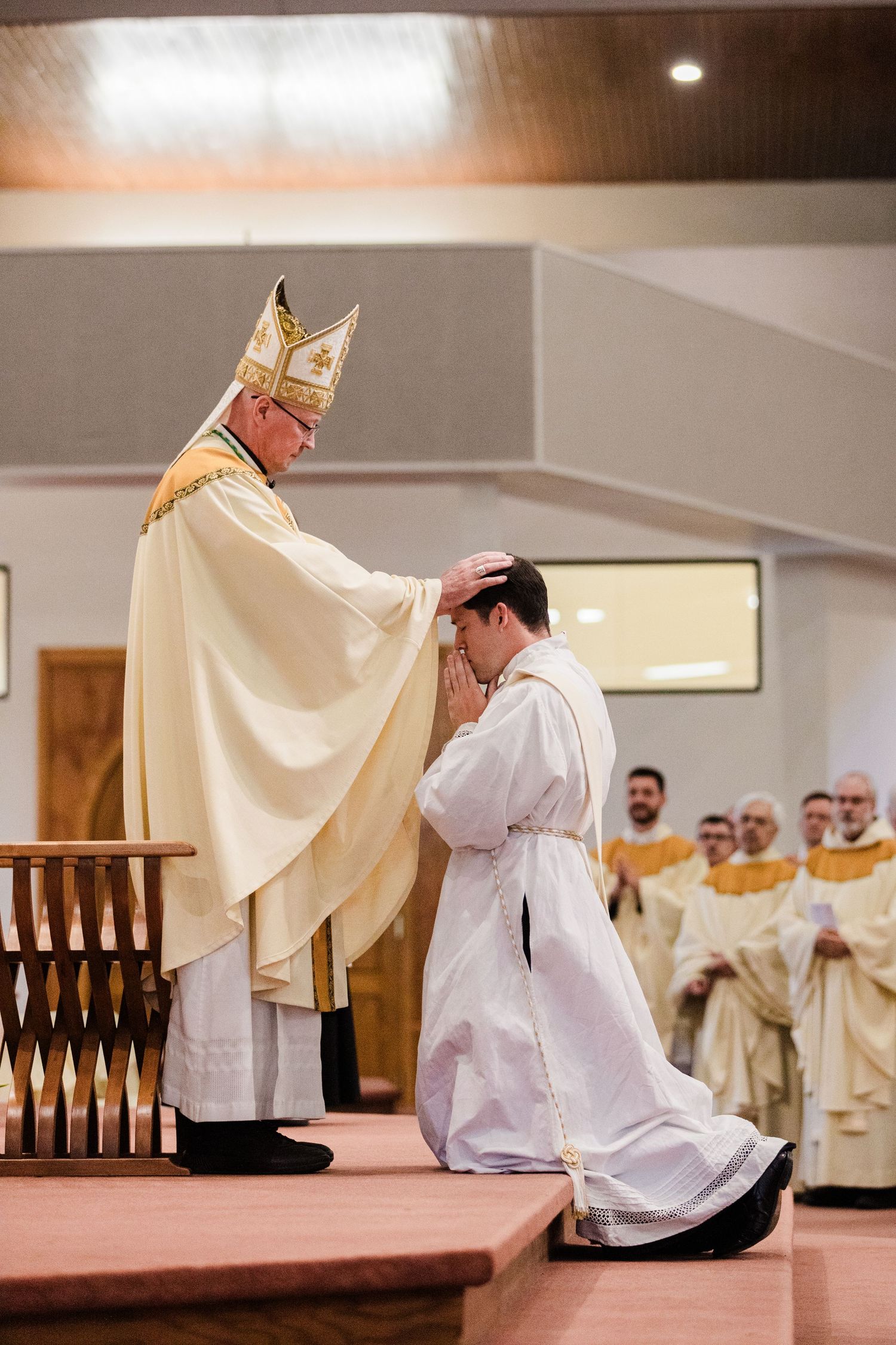 Bishop lays hands on kneeling ordinand during Catholic ordination ceremony in church.