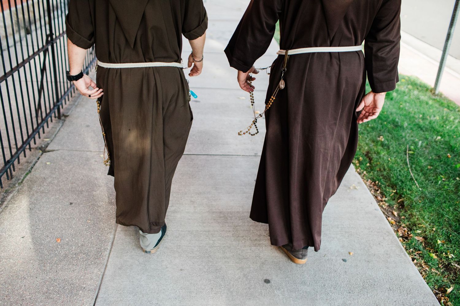 A row of brown-robed figures walking along a stone pathway next to a grassy area.