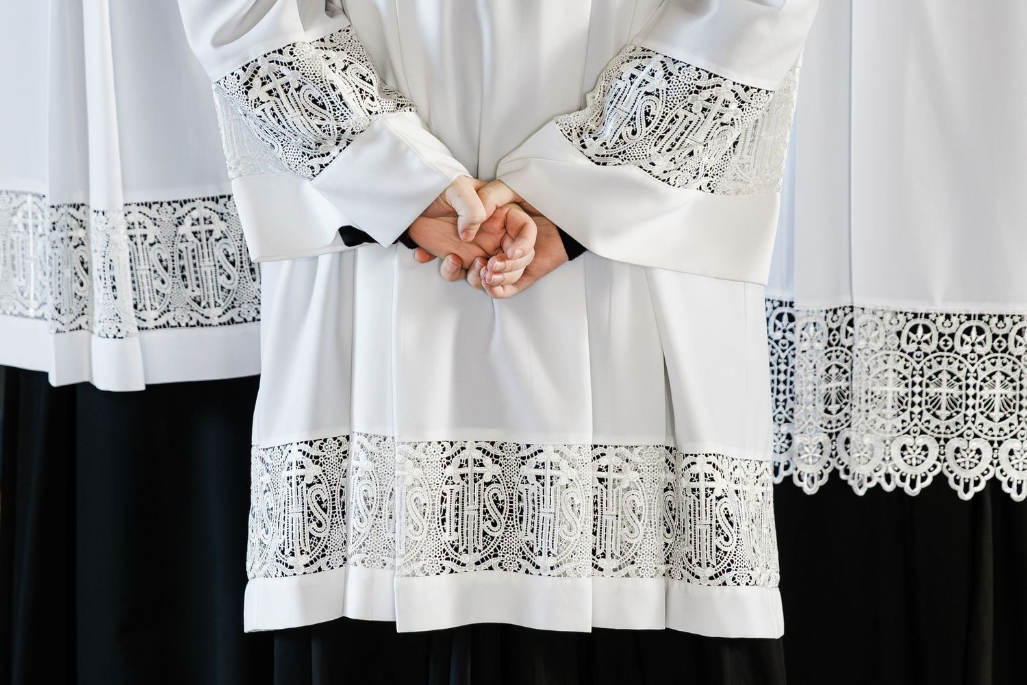Detailed white lace trim adorns the sleeves and hem of altar server vestments during a church ceremony.