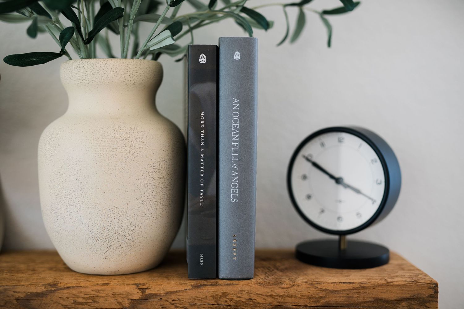 Two gray books standing upright between a ceramic vase and a round black clock.