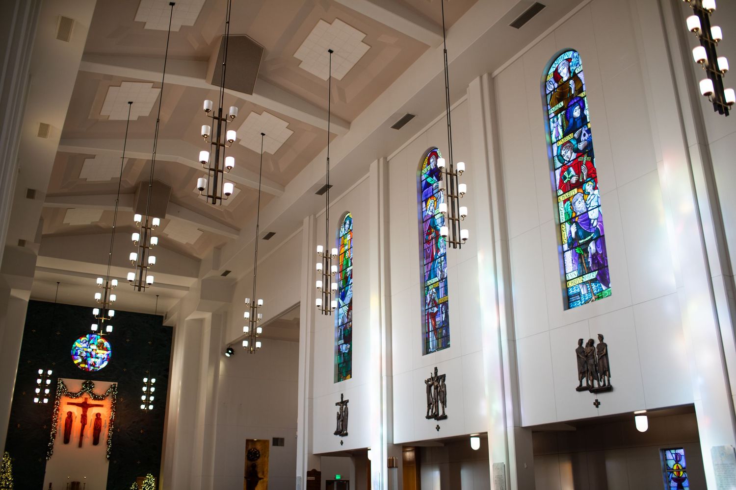 Interior view of a modern church with white walls and colorful stained glass windows along one side.