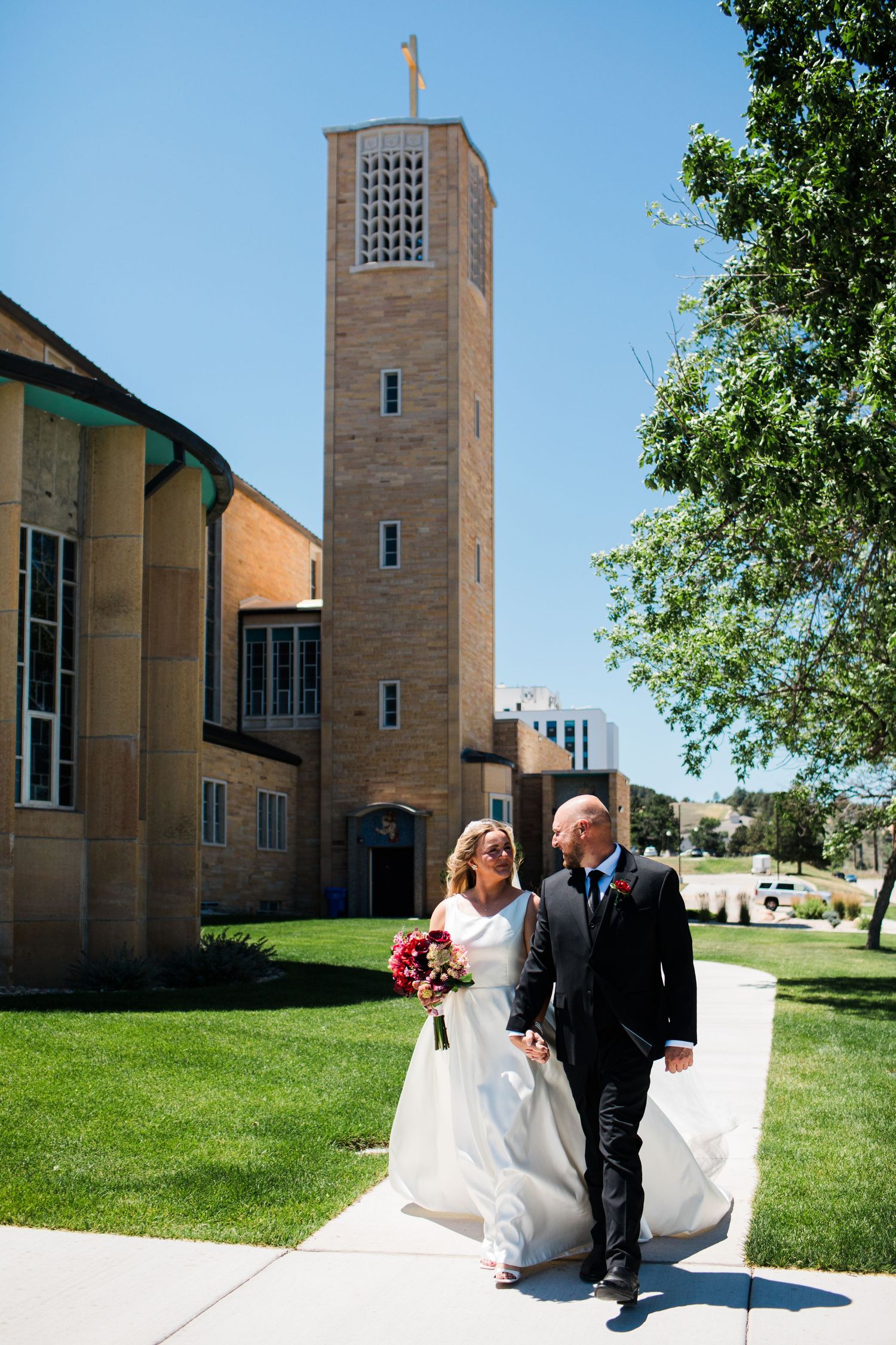 Bride and groom walking hand in hand outside a church tower on their wedding day.