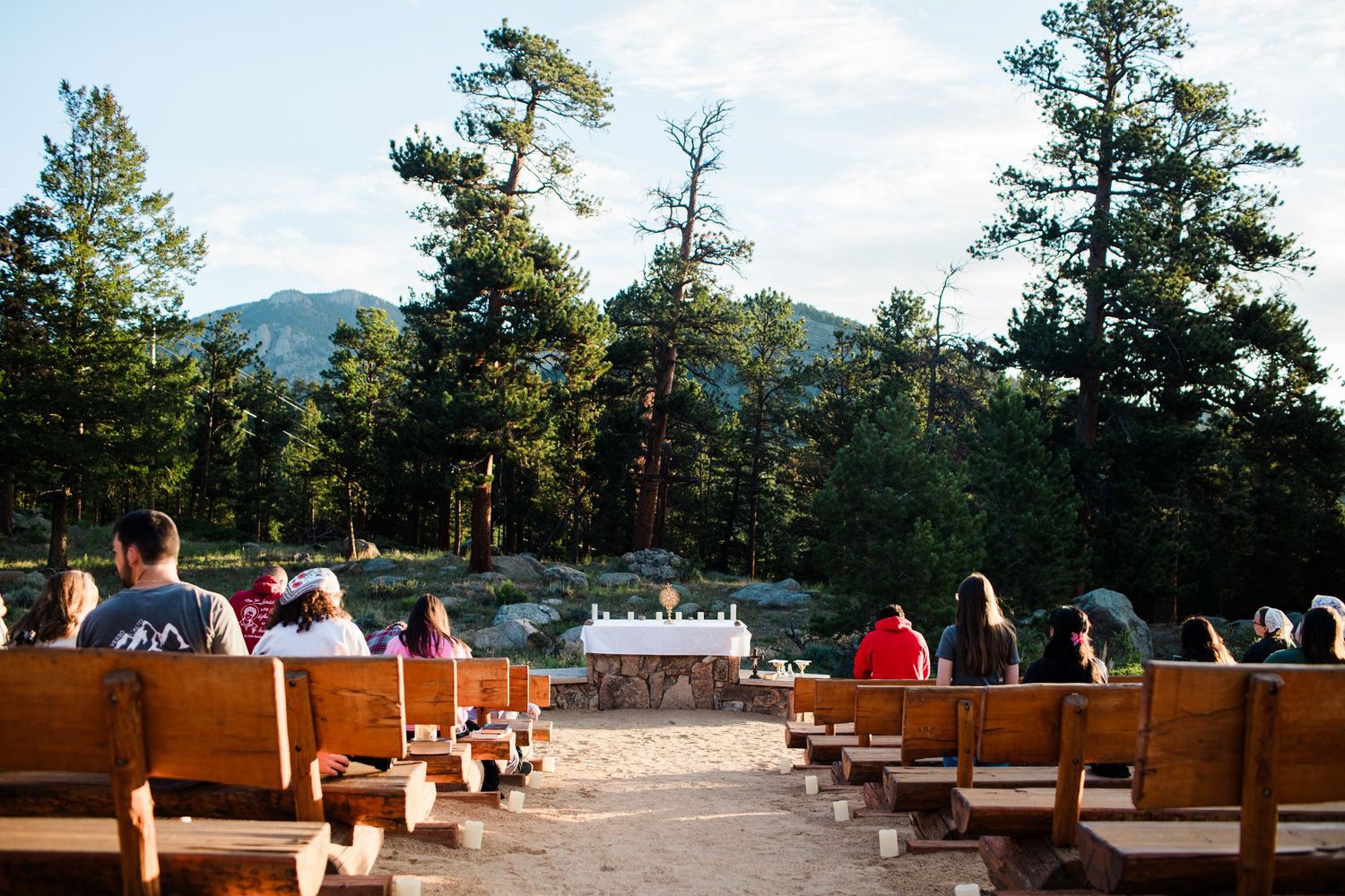 Outdoor wedding ceremony with wooden pews facing a rustic altar, surrounded by pine trees and mountain views.