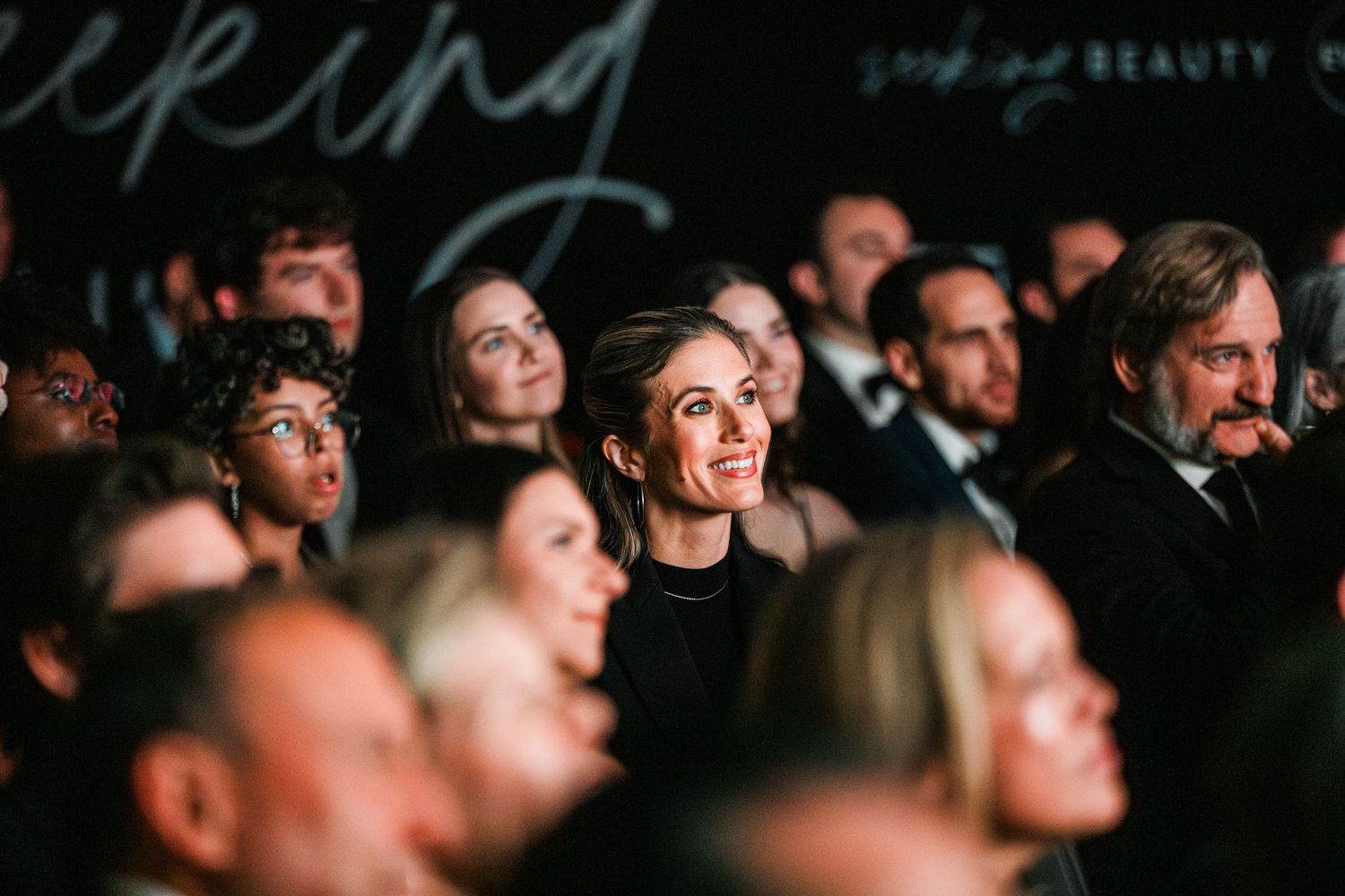 A dark audience watching intently in a crowded theater or venue.