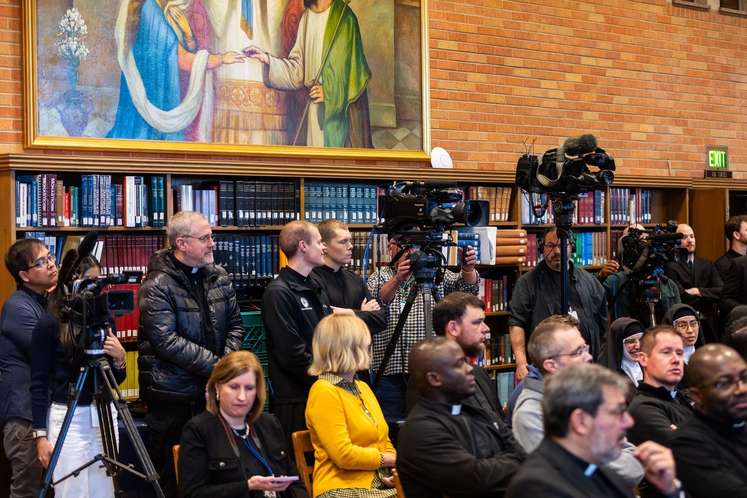 Media photographers and journalists gather in a library to cover a Catholic Church press conference.