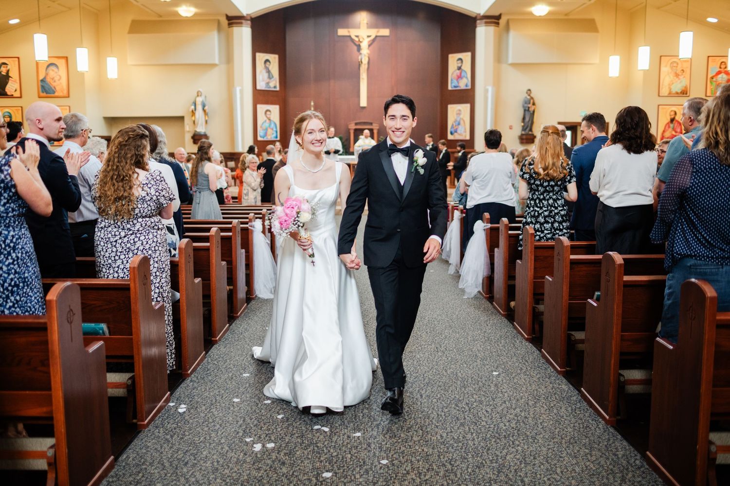 A joyful couple walks down the church aisle after their wedding ceremony while guests celebrate in the pews.