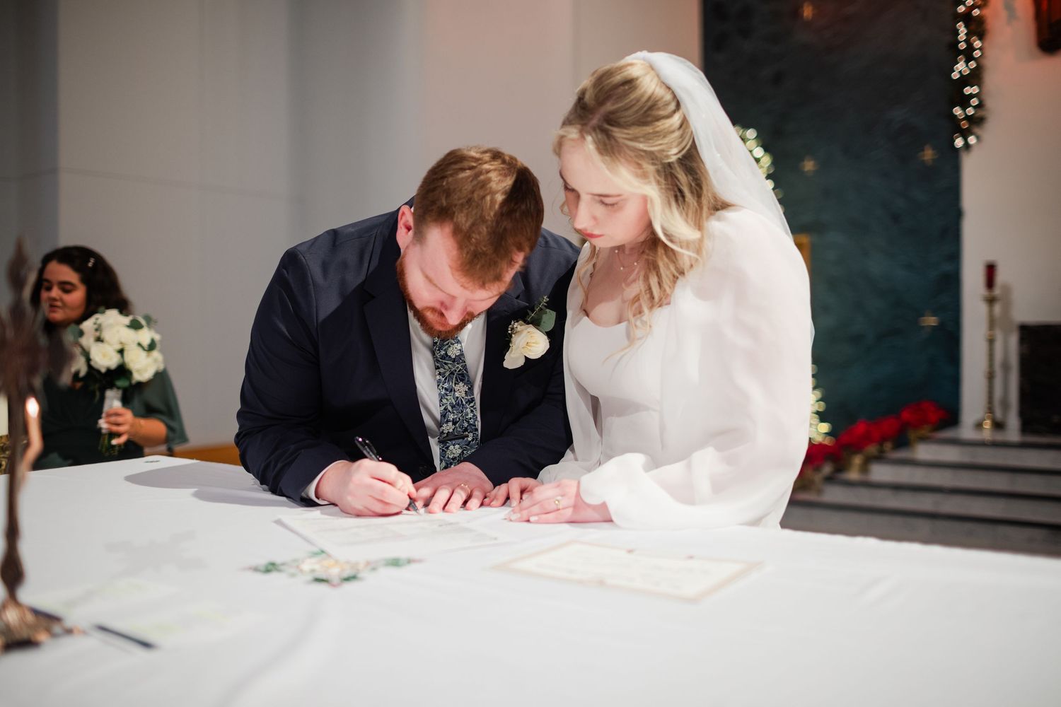 A couple signs their marriage certificate at a wedding ceremony table decorated with white linens.