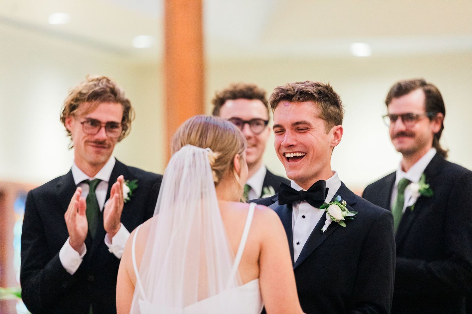 Wedding guests sharing joyful laughter and reactions during a celebration in an indoor venue.