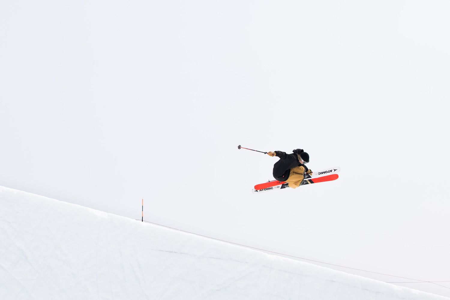 A skier performs an airborne trick against a stark white snowy background on red skis.