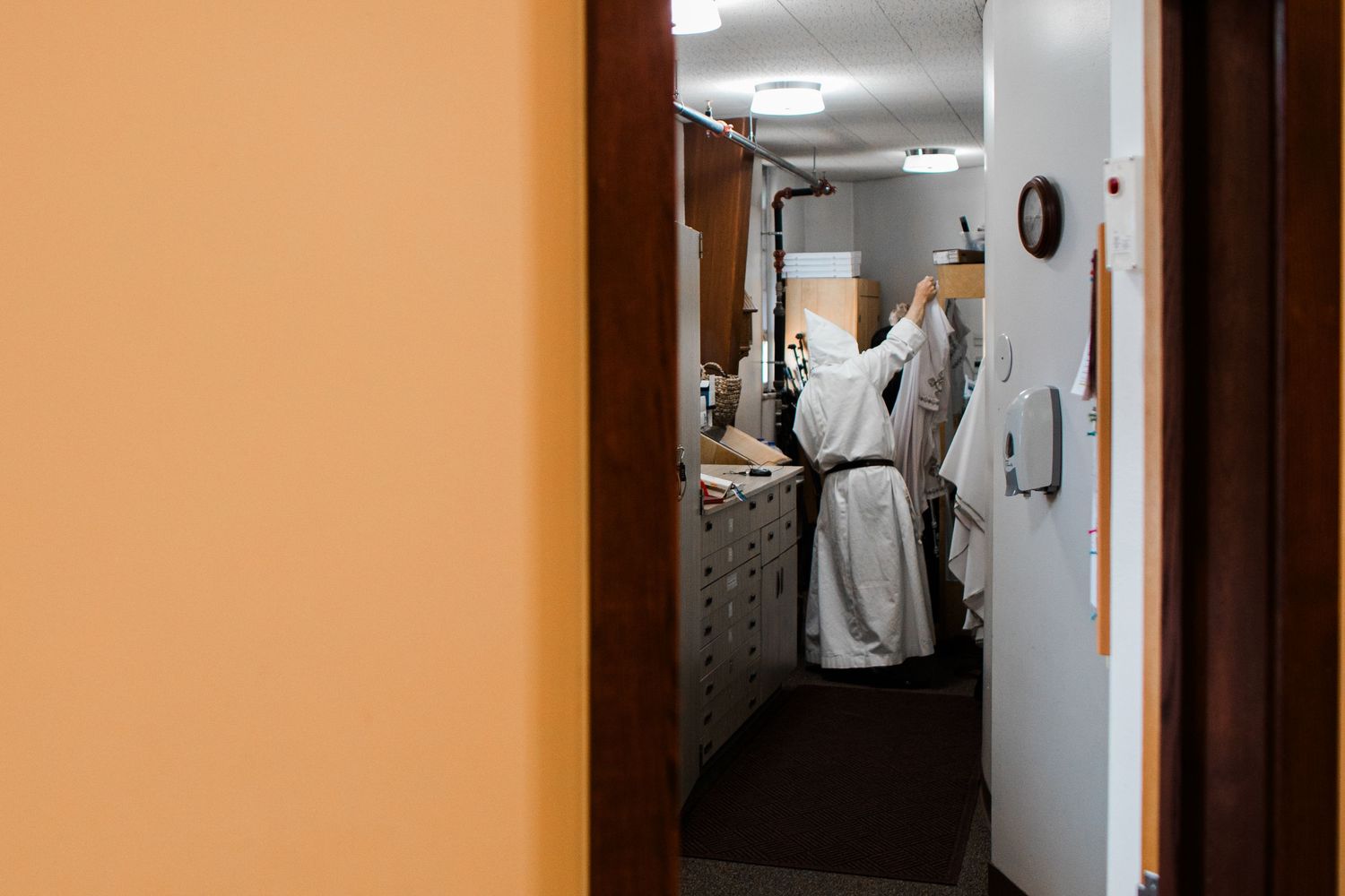 A dimly lit corridor with white walls and orange accents shows a figure walking in the distance.