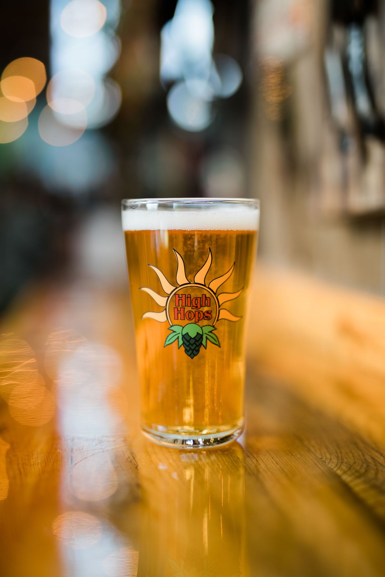 Close-up of a golden craft beer glass with foam head and brewery logo displayed on bar counter.