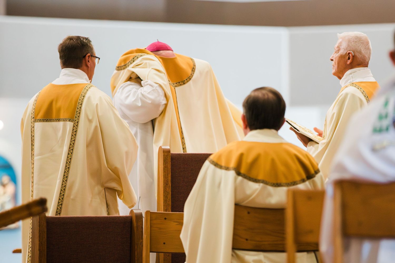Catholic clergy in white and gold vestments participate in a formal religious ceremony inside a modern church.