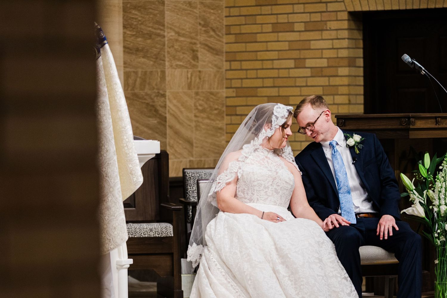 Bride and groom share an intimate moment seated together during their wedding ceremony in a church.