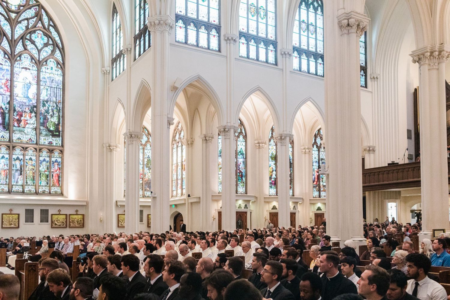 Interior view of a Gothic cathedral with high vaulted ceilings and stained glass windows during a service.