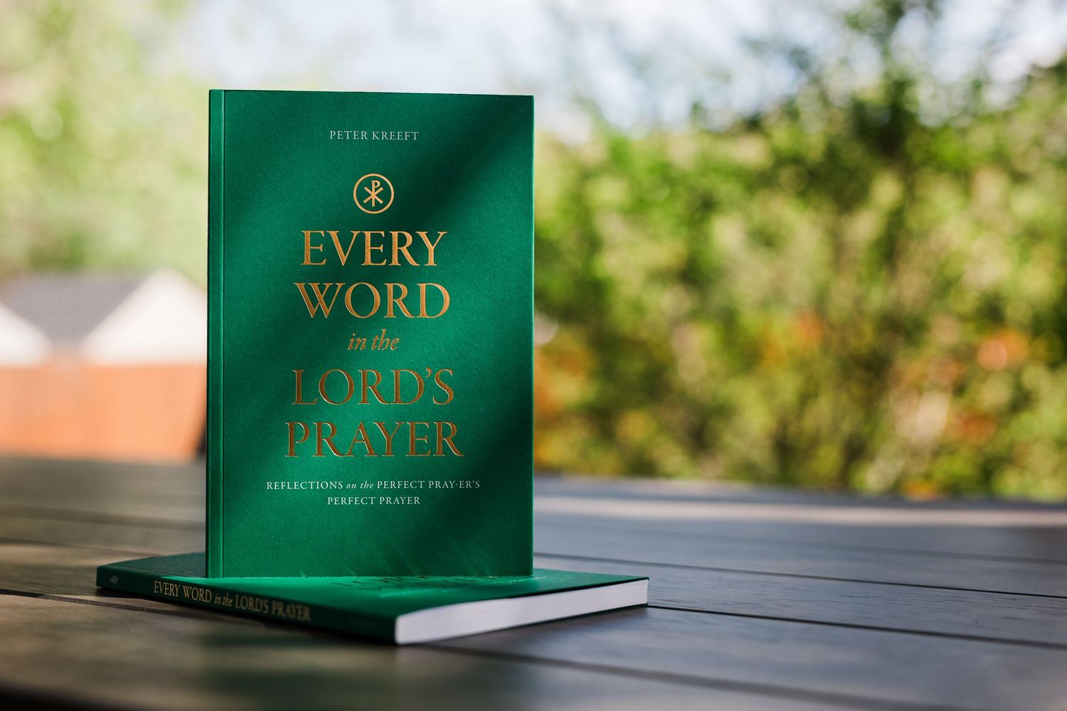 Green hardcover book 'Every Word in the Lord's Prayer' by Peter Kreeft stacked on outdoor wooden table.