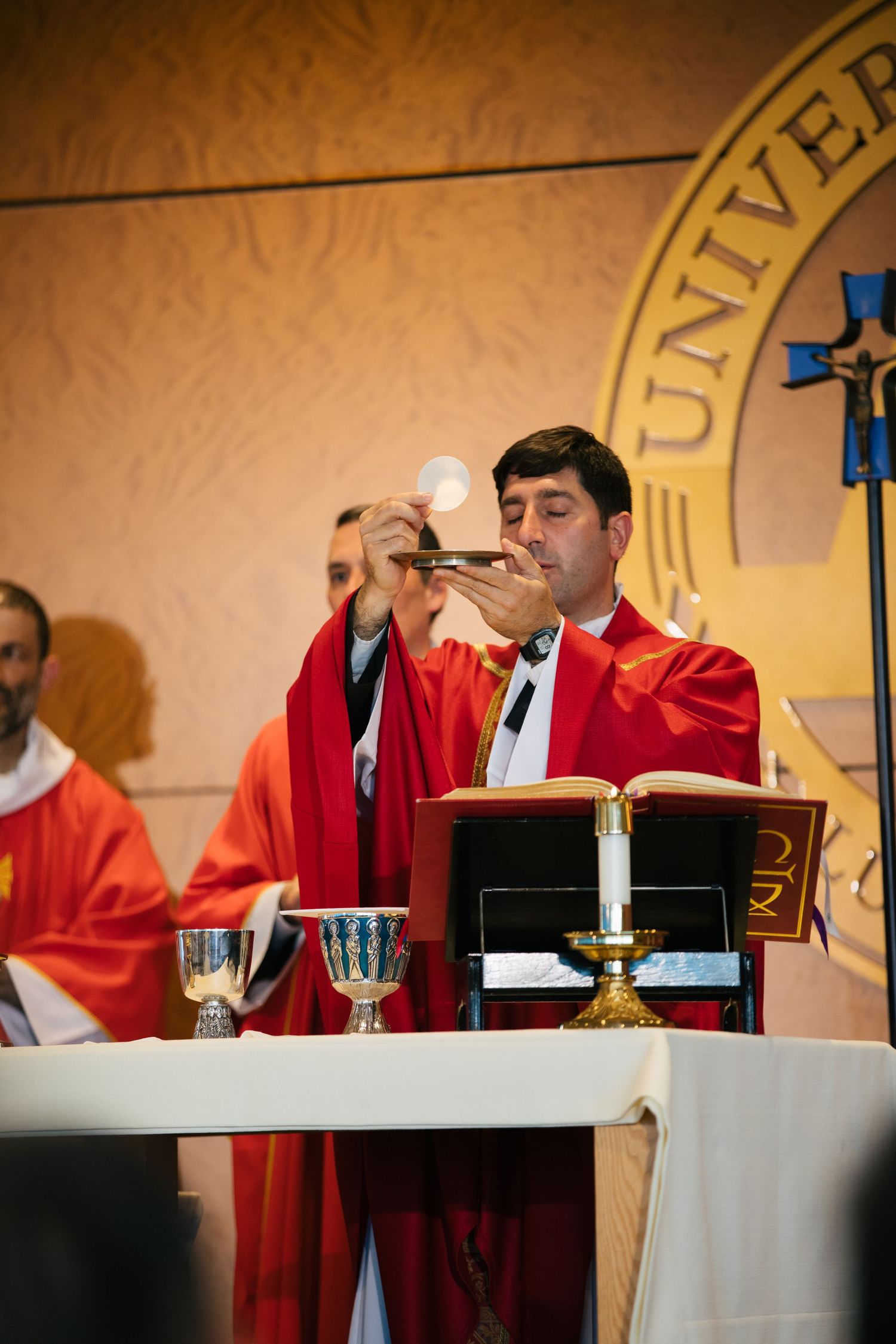 Religious leaders in red robes perform a ceremonial service at an altar with books and chalices.