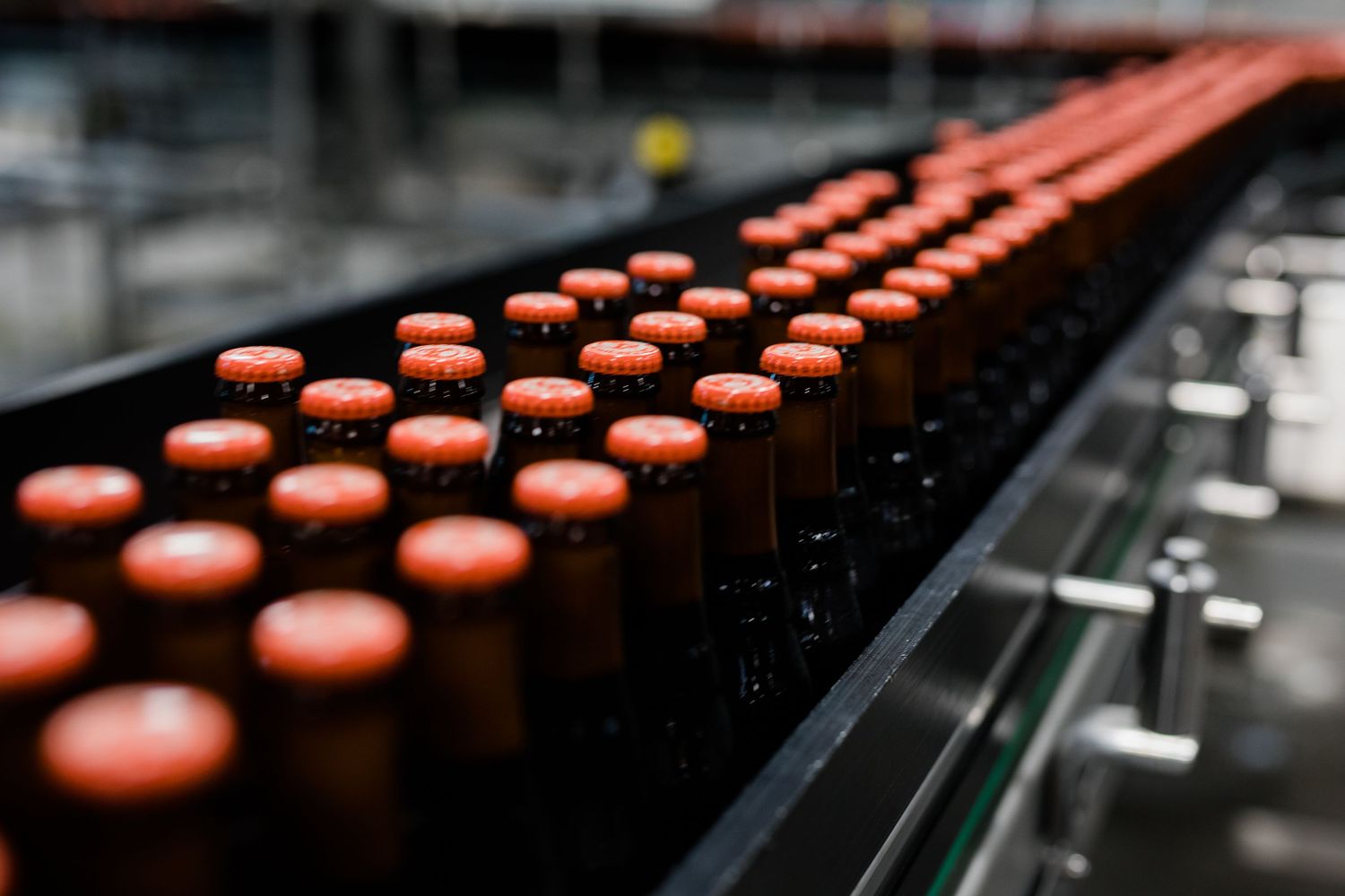 Close-up view of red bottle caps moving along a black industrial conveyor belt in a beverage production line.