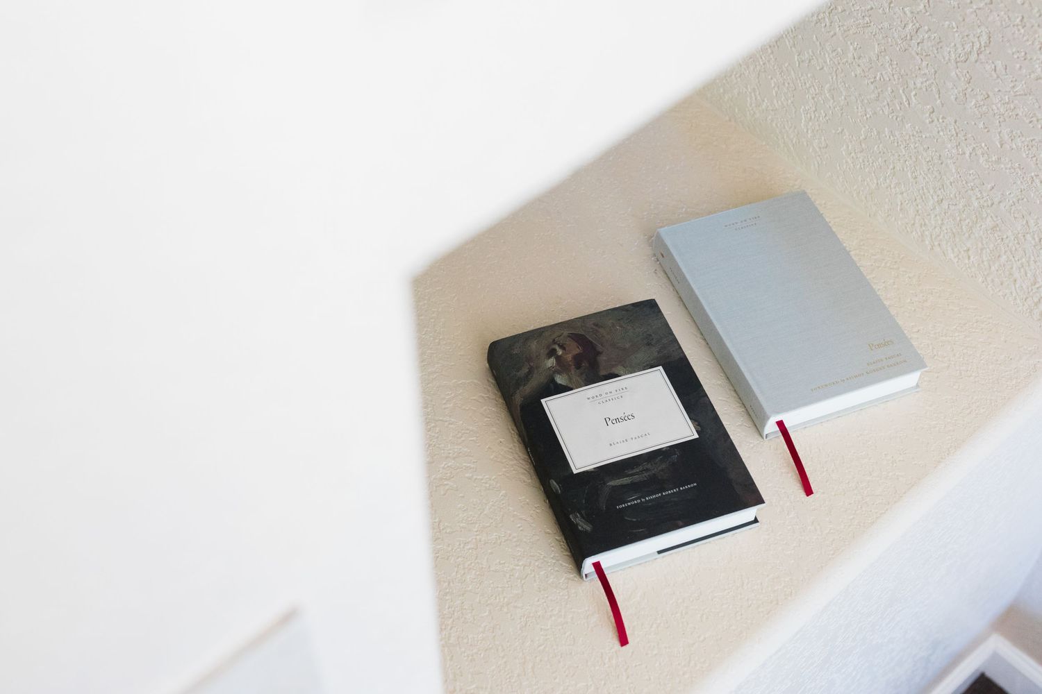 Two notebooks with red ribbon bookmarks rest on a white built-in shelf, one black marble and one silver.