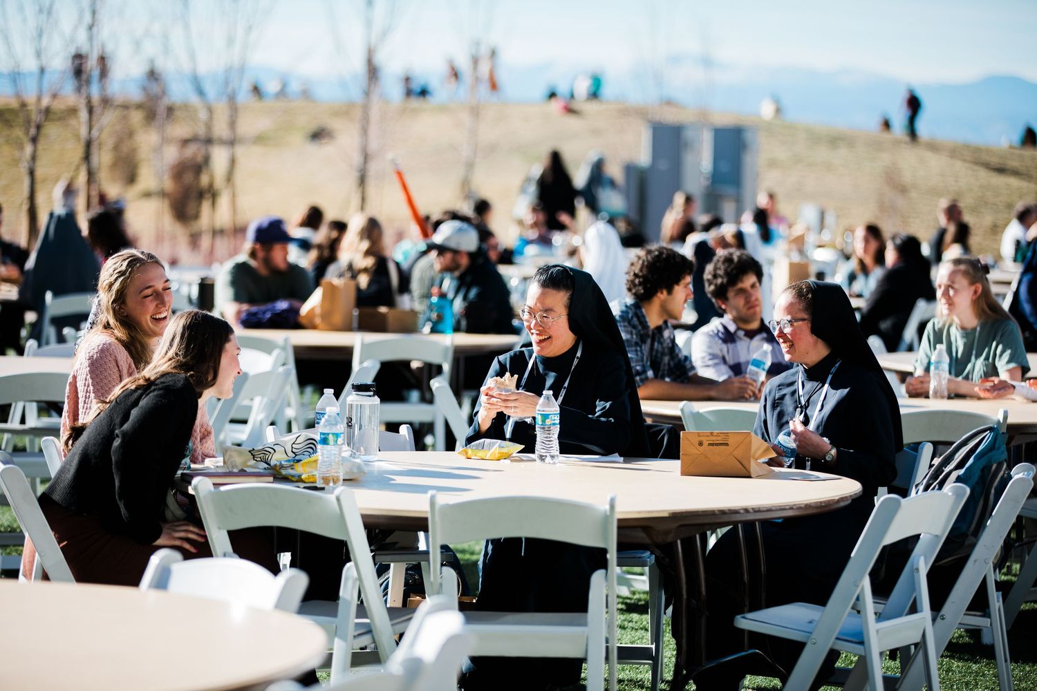 Long tables with white chairs set up outdoors for a wedding reception or celebration event.