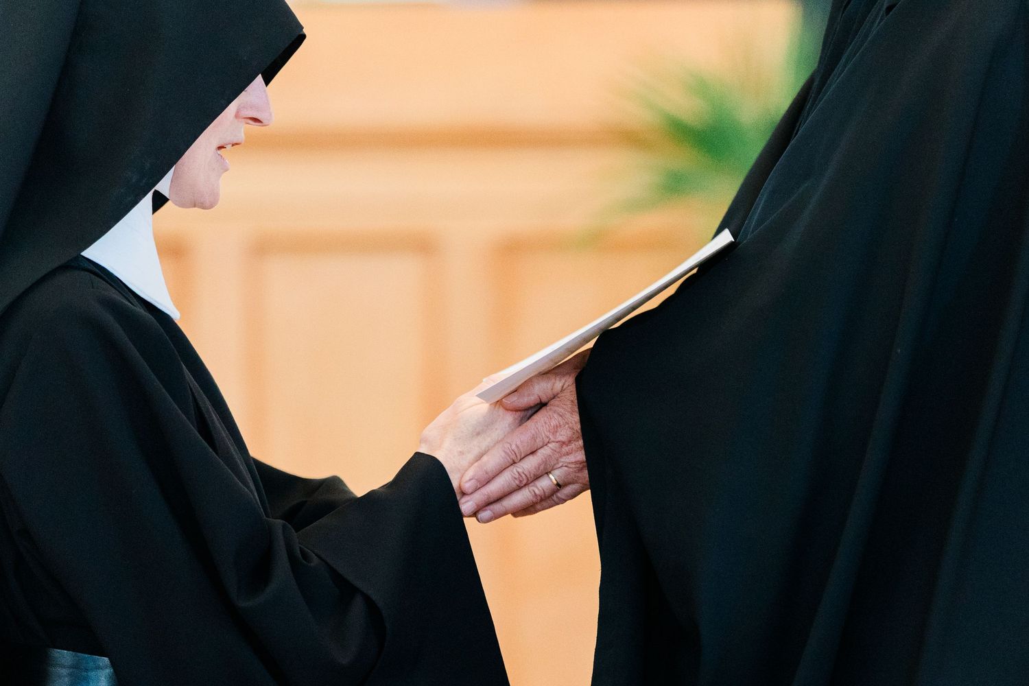Two Catholic nuns in black habits share a document in a warmly lit indoor setting.
