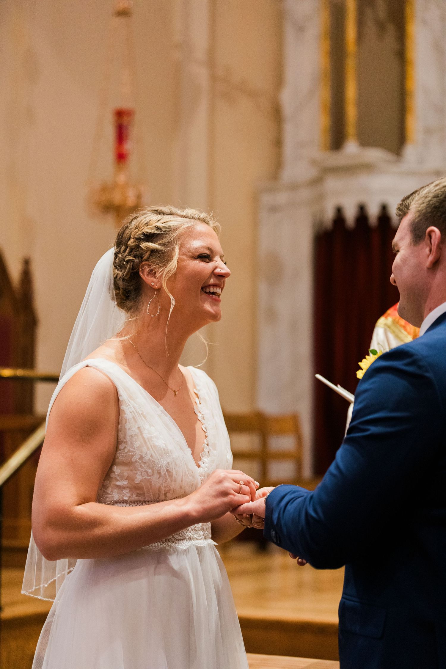Joyful bride in white gown laughing during ring exchange at church wedding ceremony.