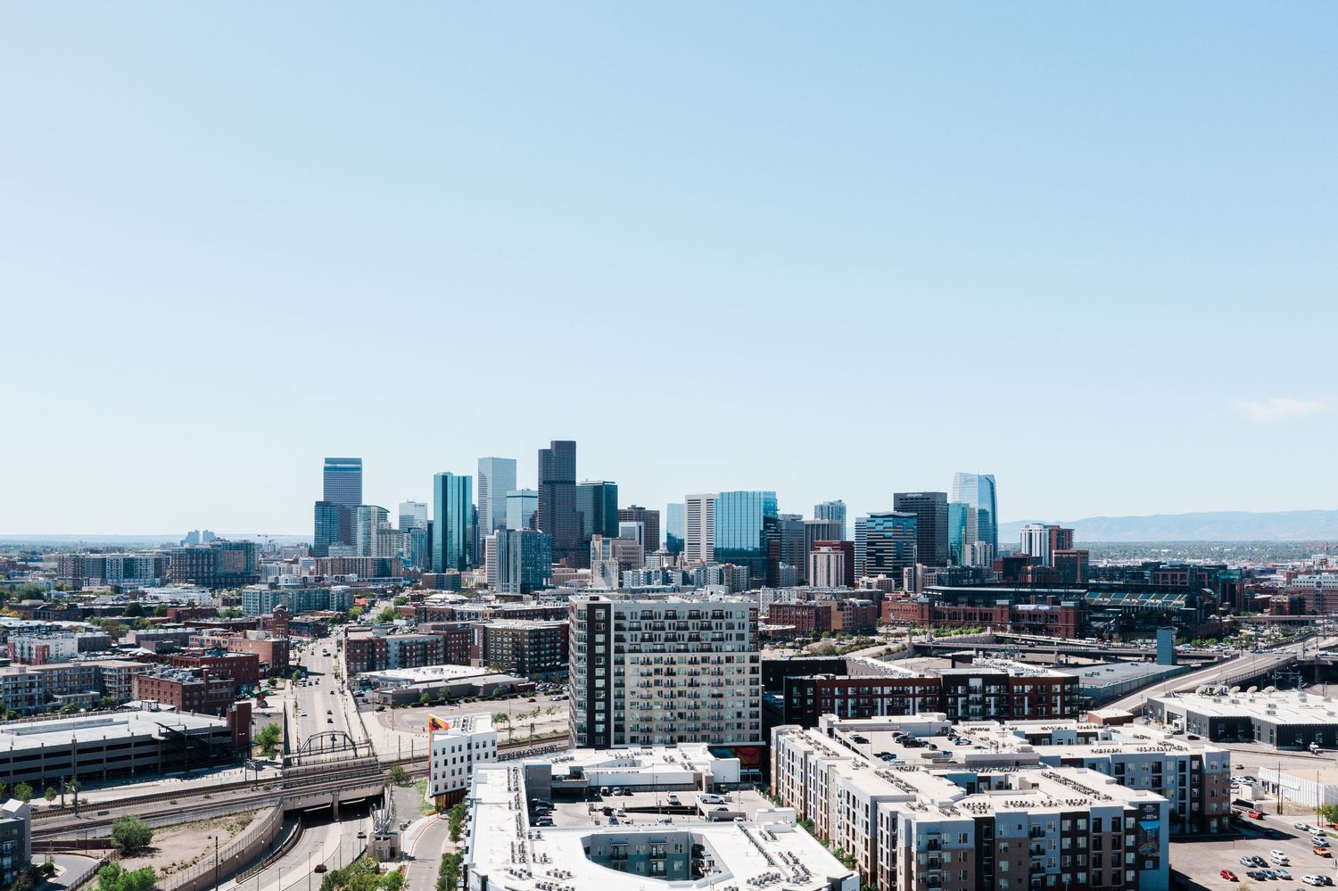 Aerial view of Denver city skyline with modern skyscrapers under a clear blue sky on a sunny day.