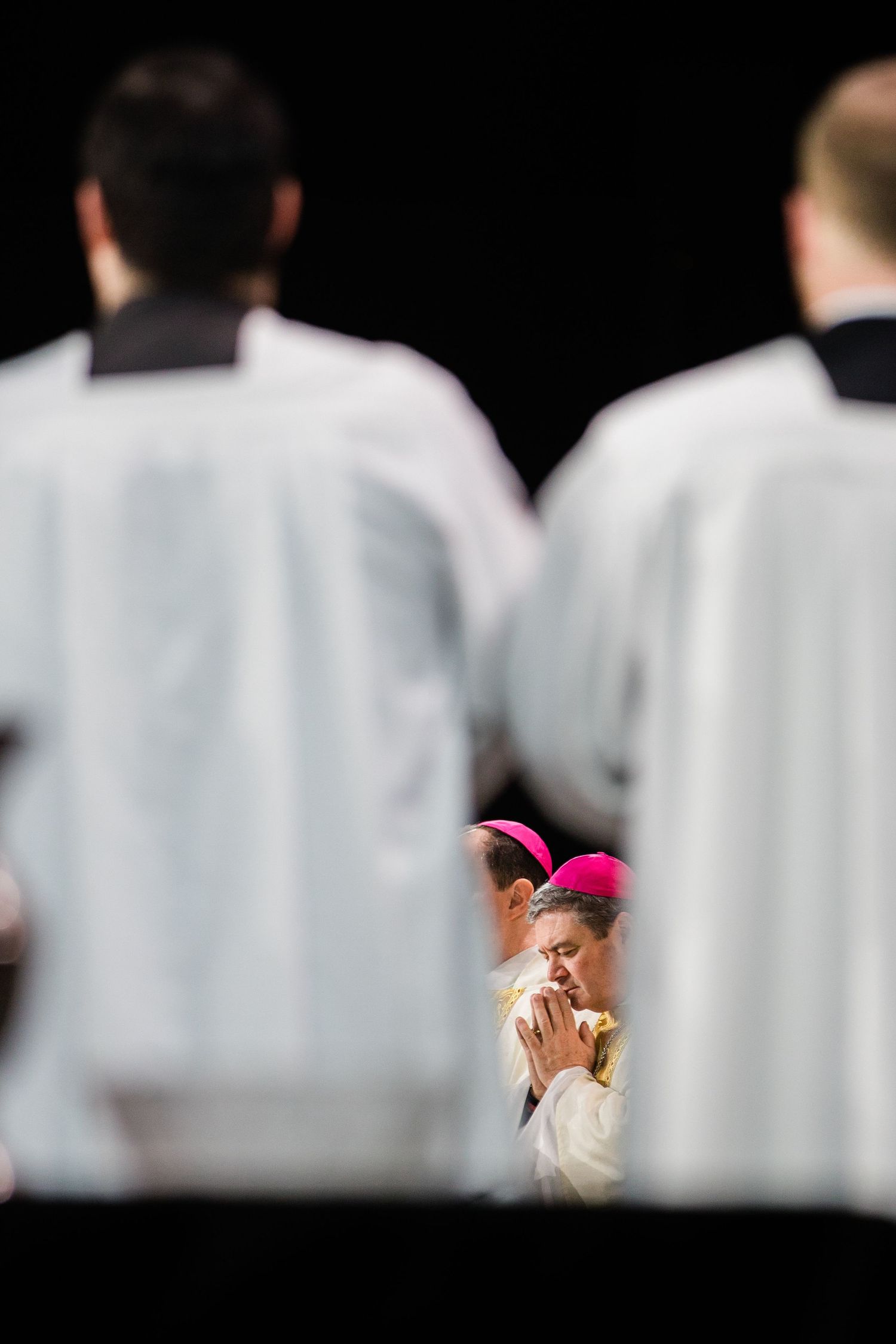 Row of white-robed choir members with pink clerical accessories visible.