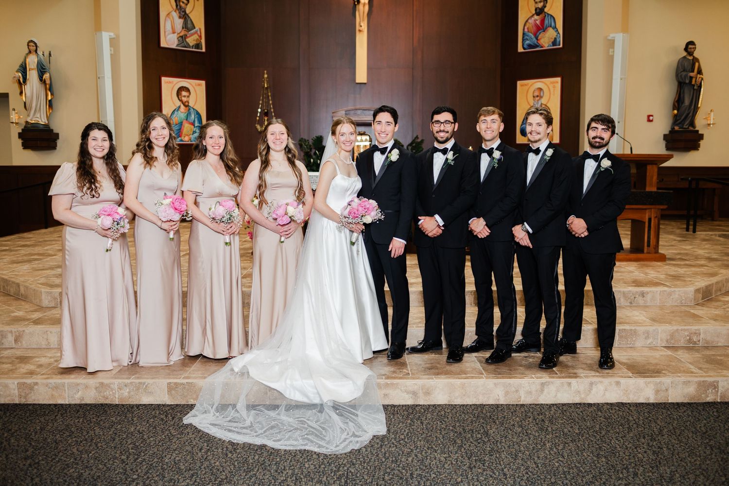 Wedding party members in formal attire pose elegantly in a grand indoor venue with ornate decor.