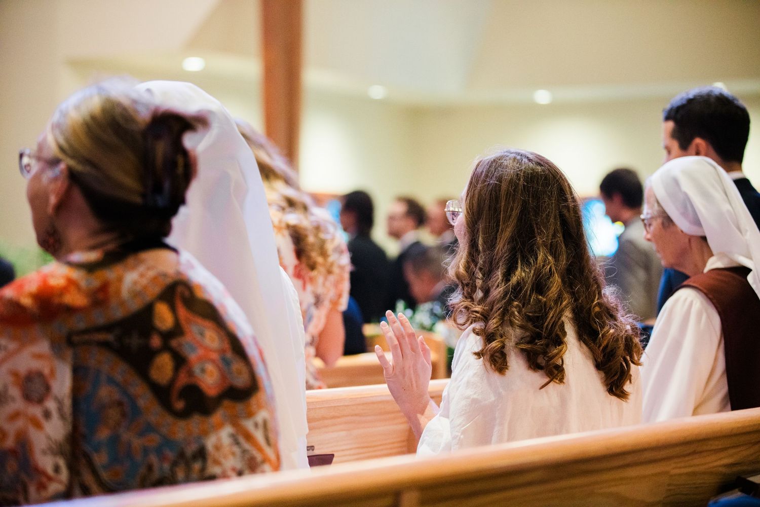 People seated in wooden church pews during a religious ceremony.
