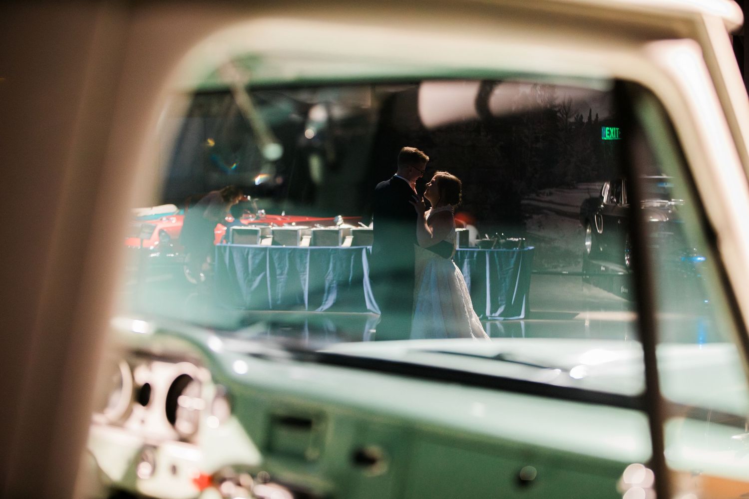 Bride and groom share a romantic moment reflected through a vintage teal truck window at their wedding reception.