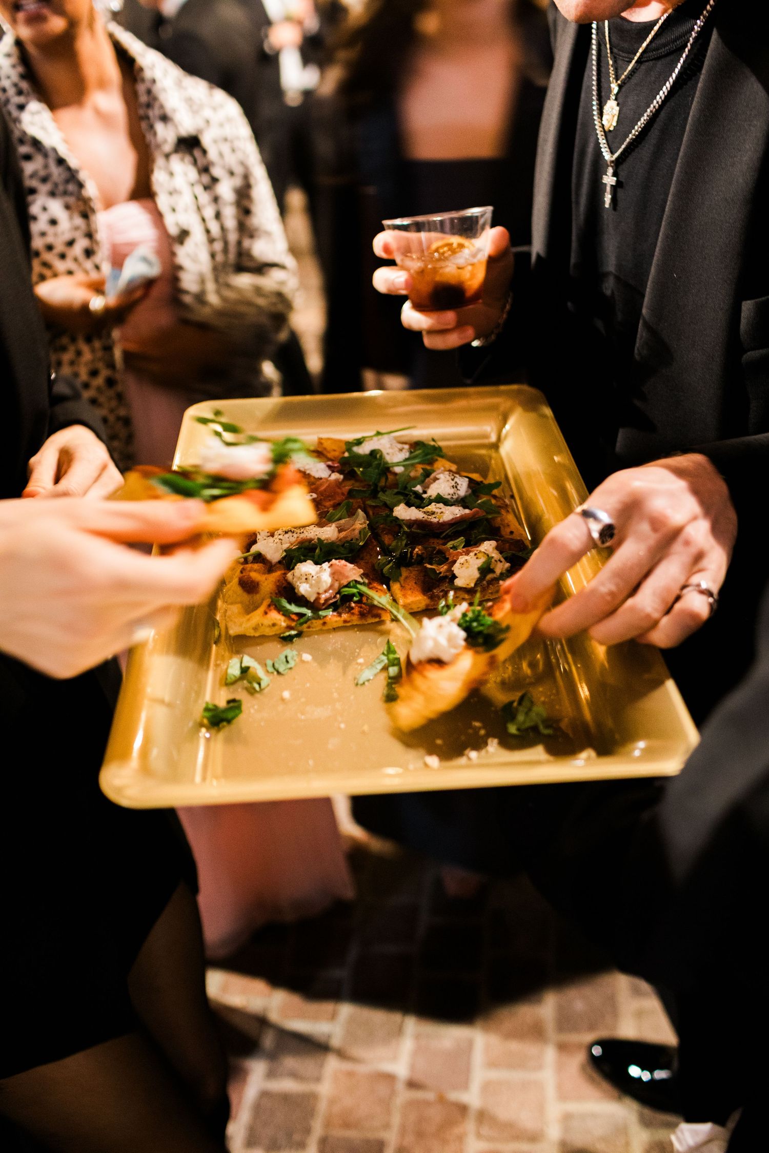 Close-up of hands holding golden serving plates with gourmet food at an upscale catering event.