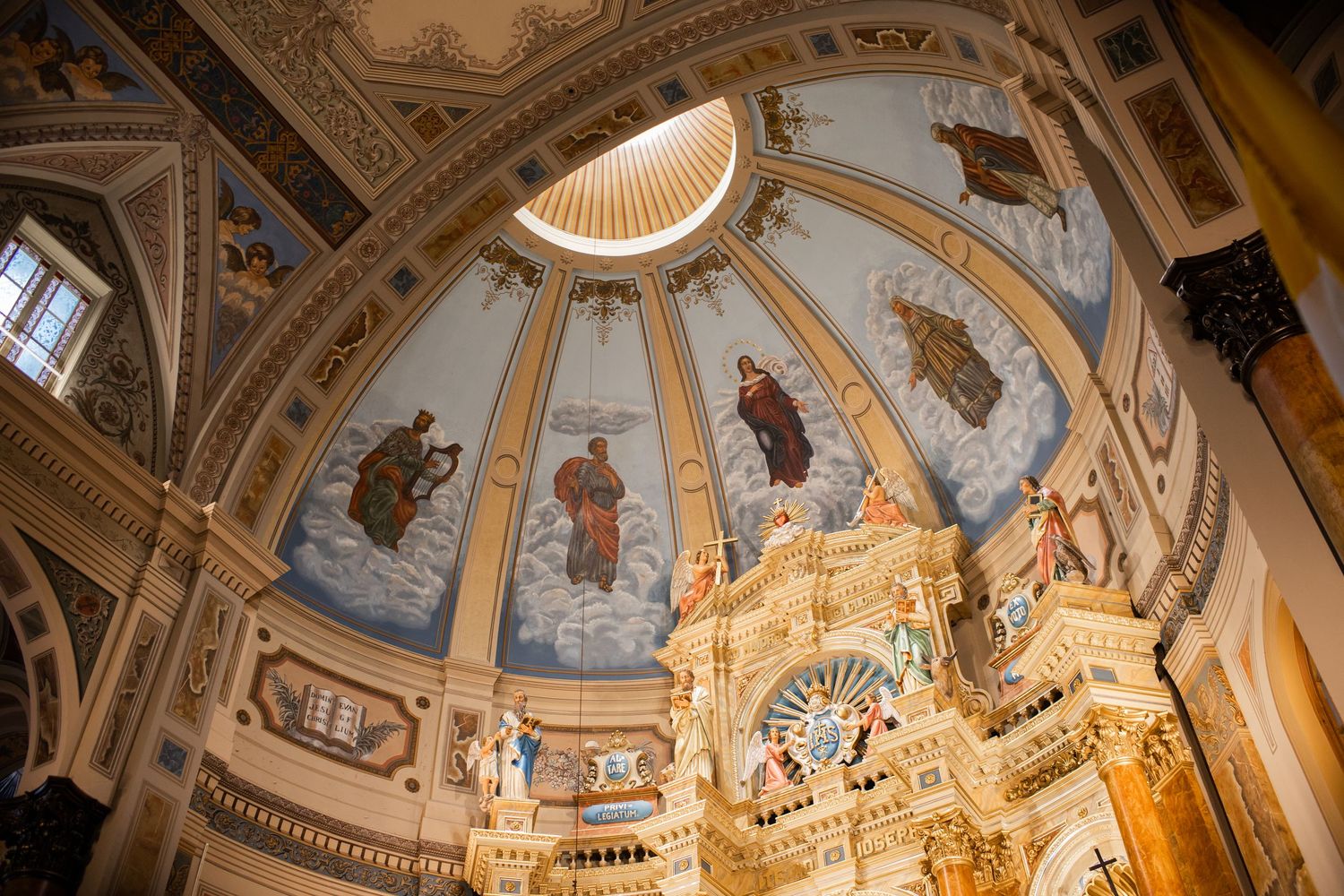 Ornate cathedral dome with religious frescoes and golden details illuminated from above.