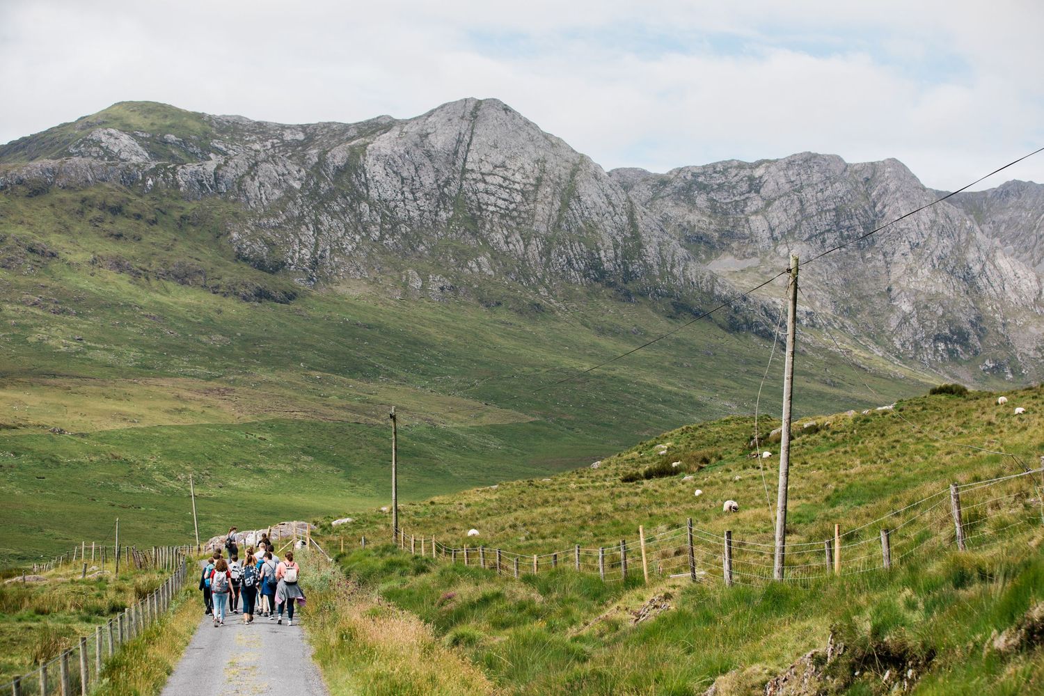 Group of pilgrims walking along a narrow rural road with dramatic Irish mountains in the background.
