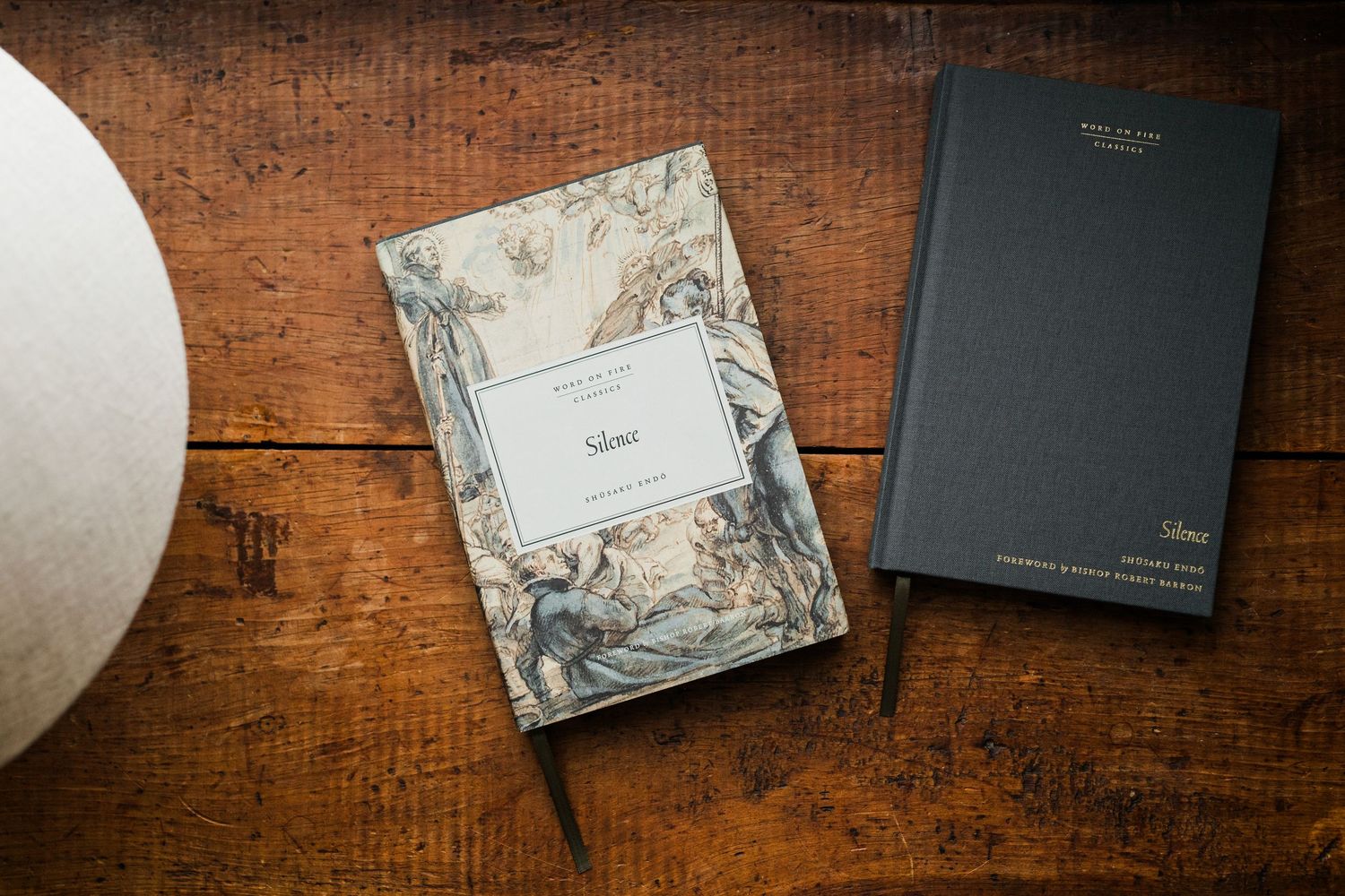 Two elegant journals on a wooden table, one with botanical art cover and one black hardcover notebook.