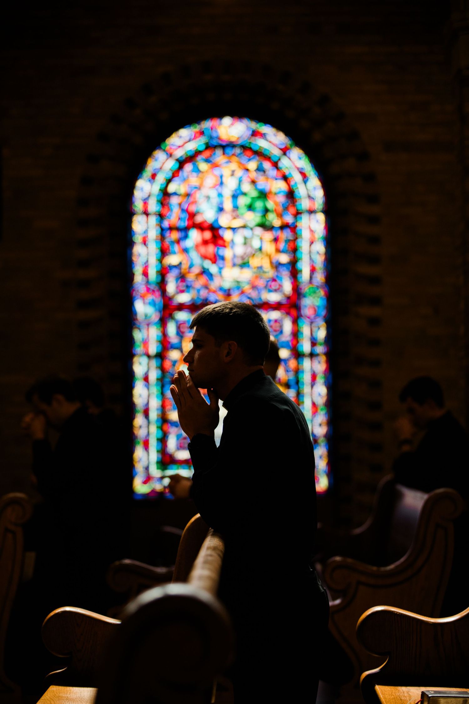 A silhouette in prayer against a colorful stained glass church window during a service.