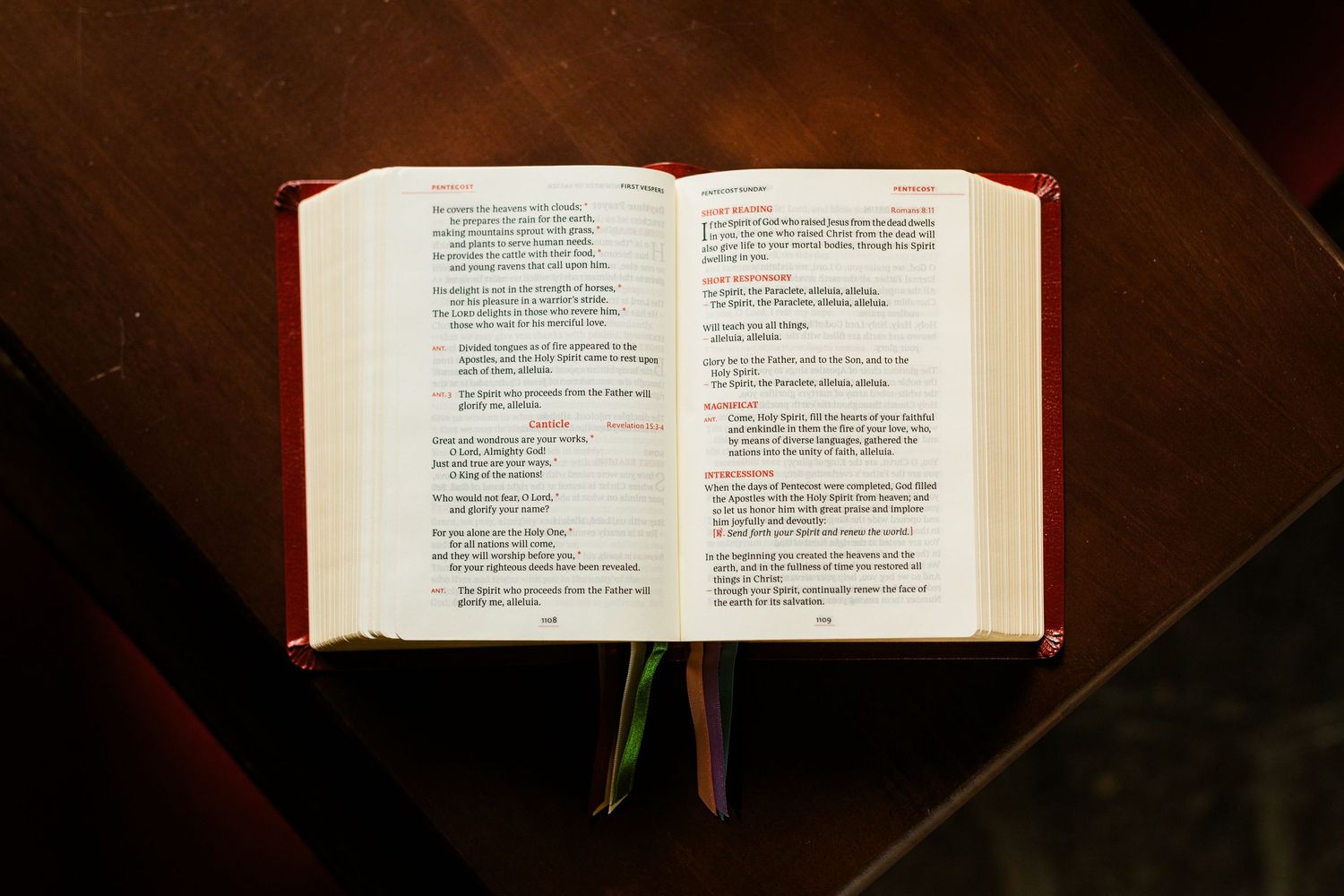Open red Liturgy of the Hours book displaying two columns of prayer text on wooden surface.
