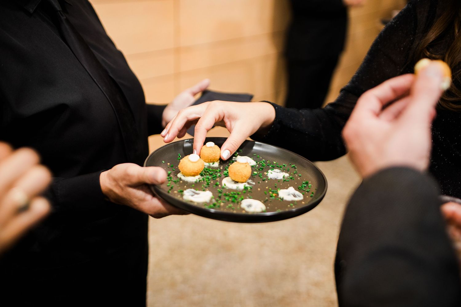 A person's hands holding a small plate with an elegantly plated appetizer garnished with microgreens and edible flowers.