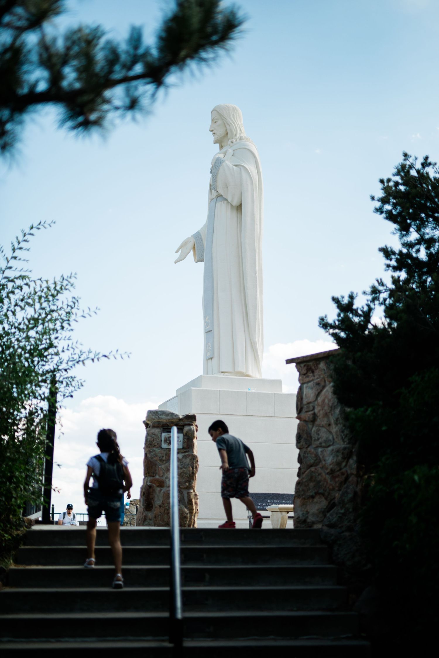 White statue stands against blue sky as visitors climb stone steps.