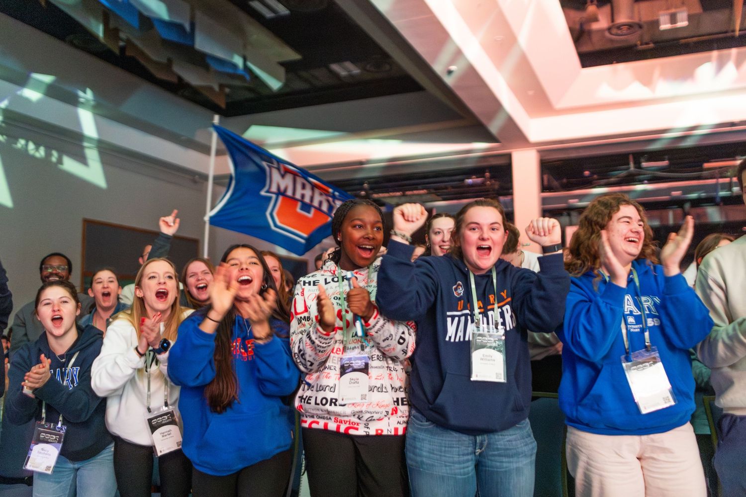 A group of people wearing blue shirts react with excitement and enthusiasm at what appears to be a conference event.