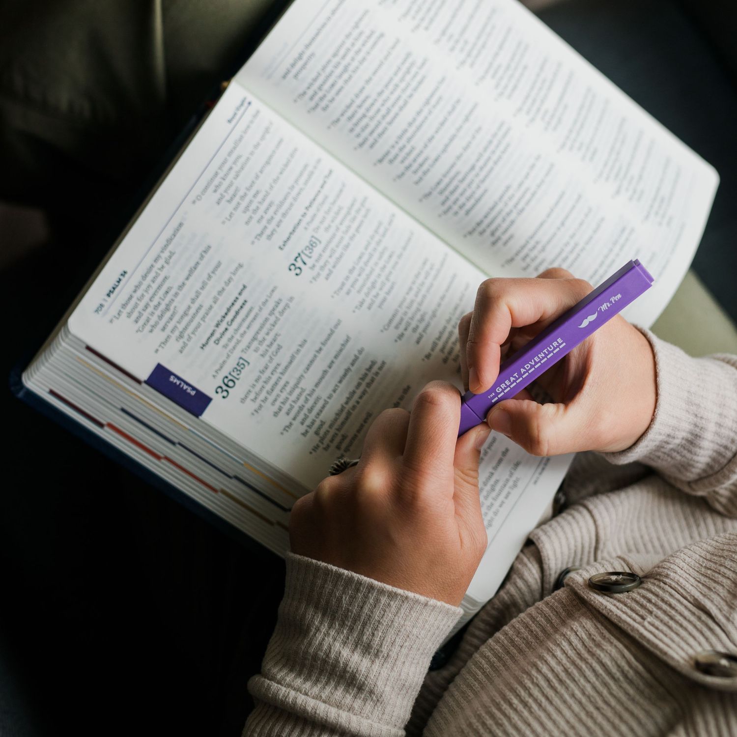 Student highlighting and taking notes while reading a textbook with a purple pen on a dark background.