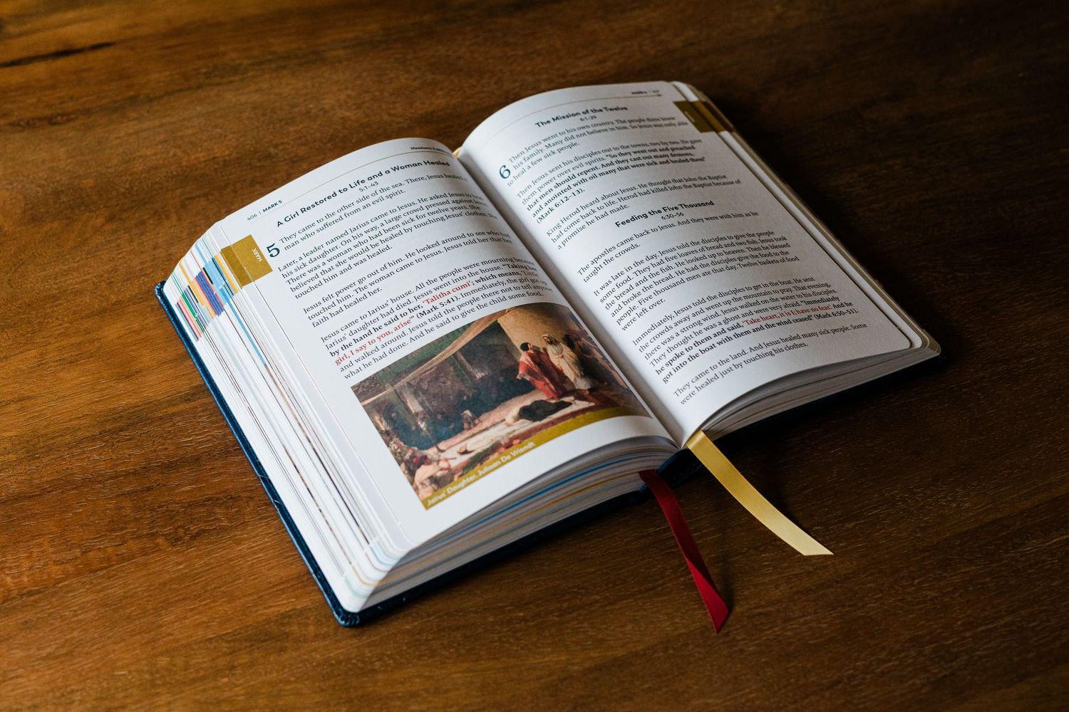 Open hardcover book with colorful bookmarks resting on a wooden table, featuring text and an image on its pages.
