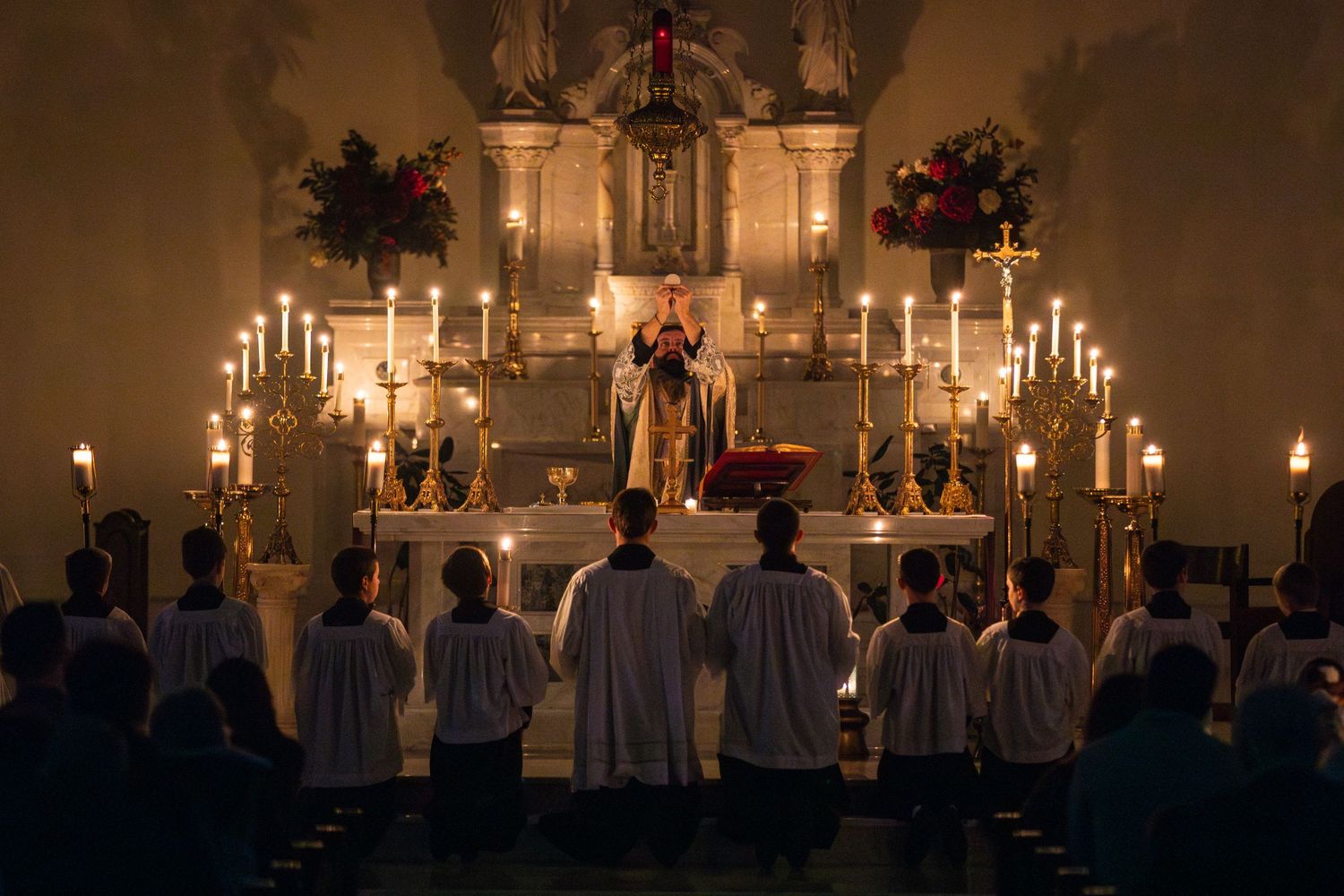 Candlelit altar during traditional Catholic mass with priests in white robes.