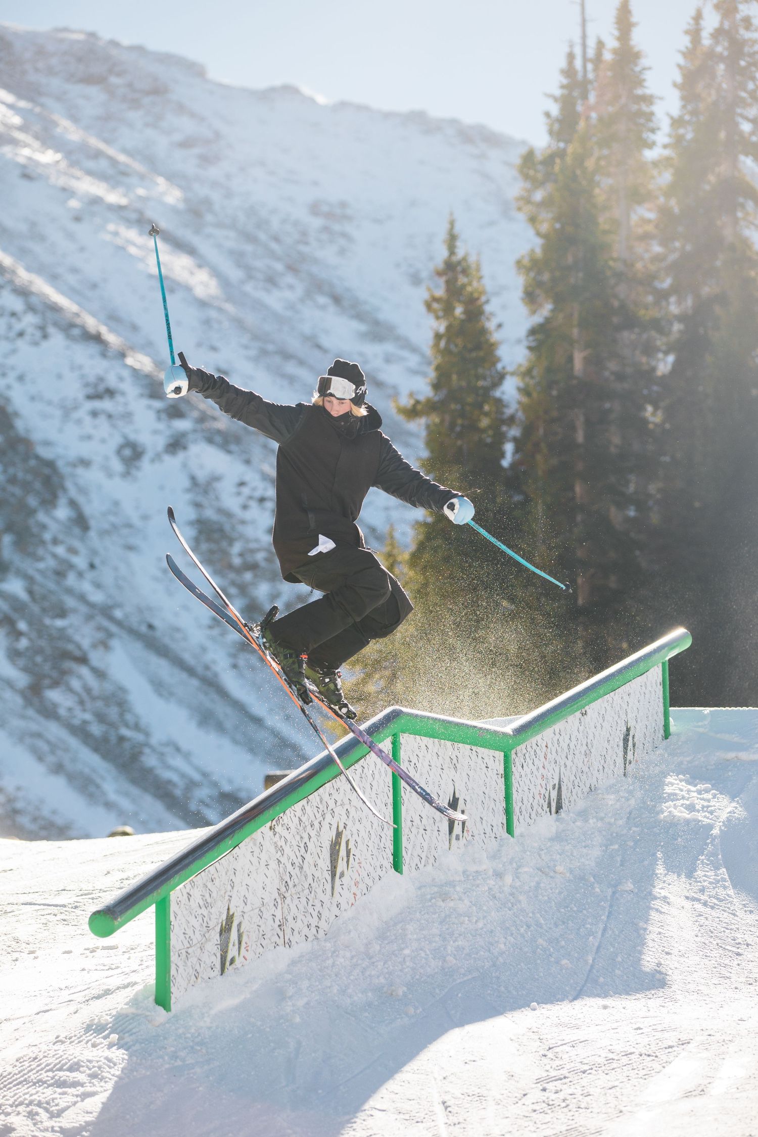 Skier executing an aerial trick off a snow park rail against a mountainous backdrop.